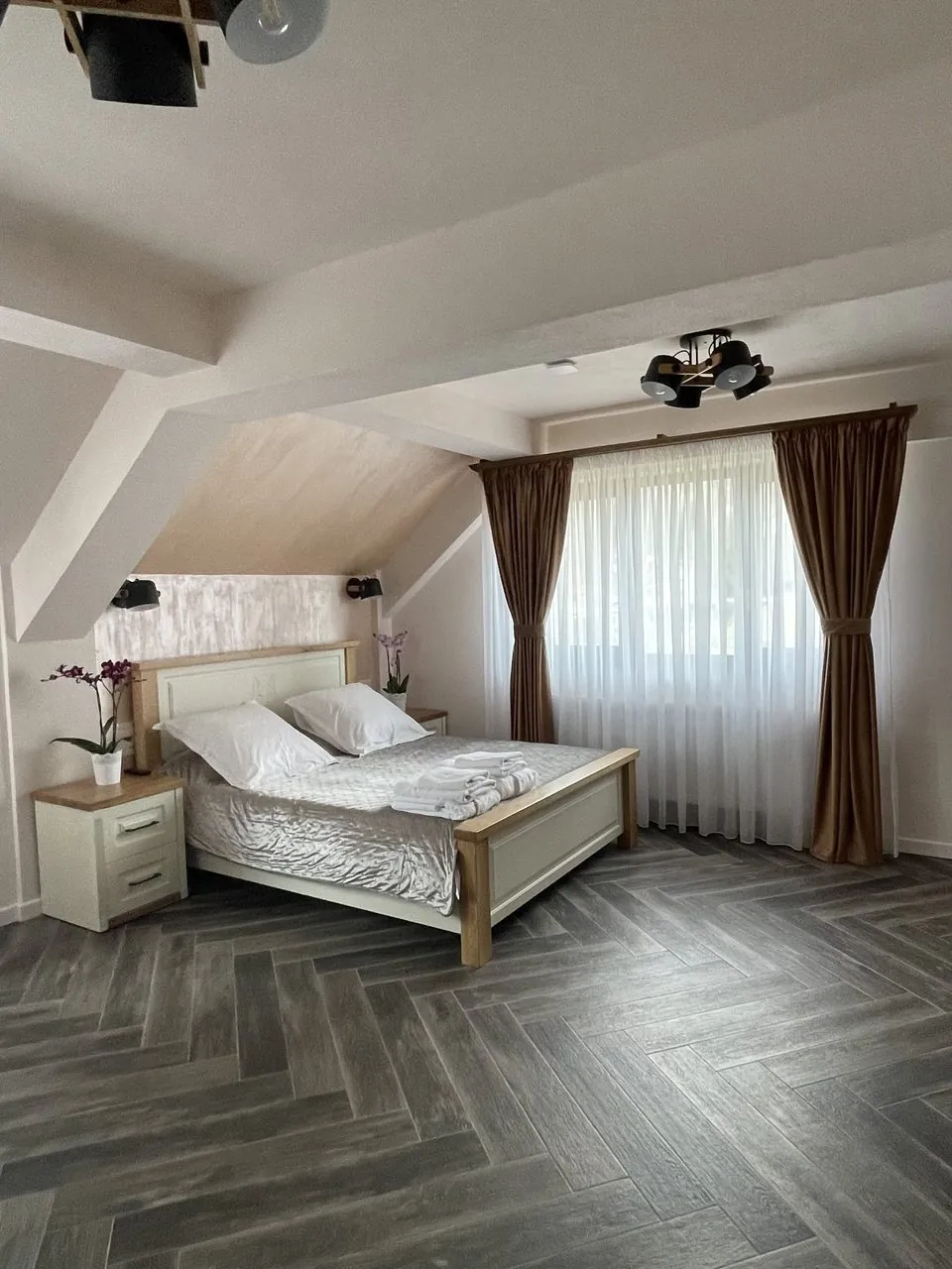 Dormitor mansardat cu pat crem și draperii