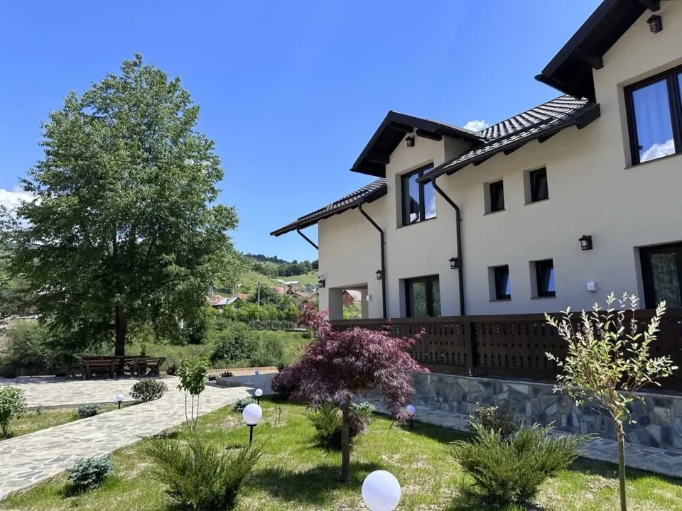 Exteriorul vilei Hanul cu Brazi vara — fațadă albă cu balcoane din lemn și grădină amenajată