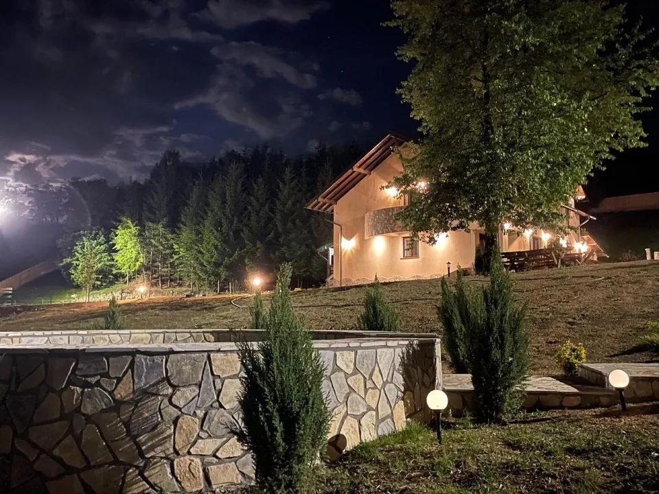 Vila Hanul cu Brazi noaptea, luminată cald, cu zid de piatră și brazi